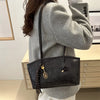 A person is holding a black leather tote bag with gold hardware and a long chain strap, worn over a light gray sweater.