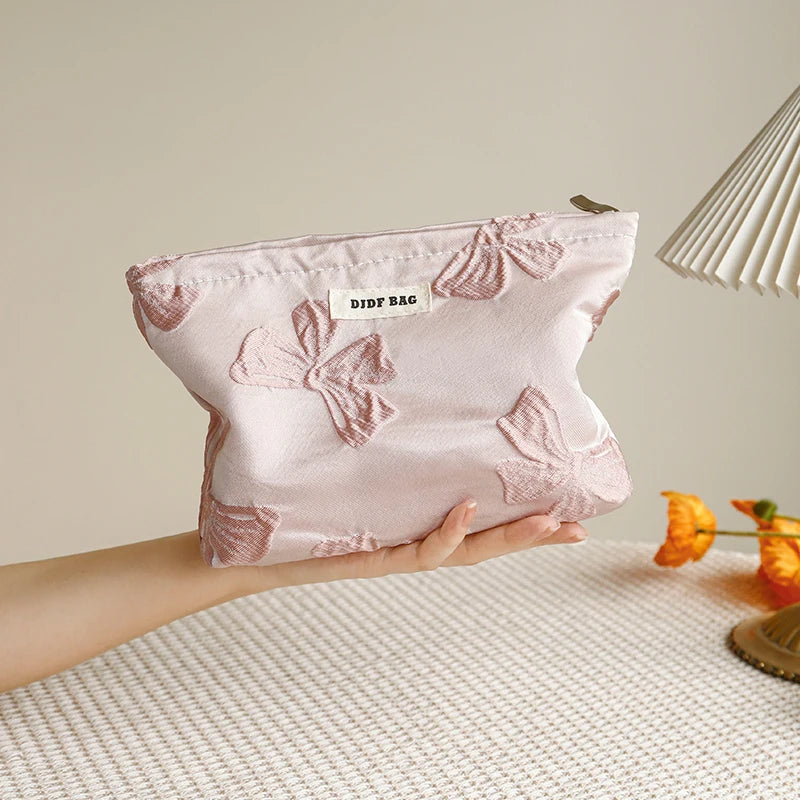 A pink floral canvas makeup bag is held in a hand against a light background.
