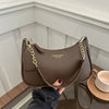 A brown leather shoulder bag with a gold chain detail is held against a white paneled background.