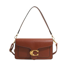 A brown leather shoulder bag with a gold initial detail and thin strap.
