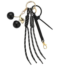 A pink cherry charm bag keychain featuring a gold-colored charm and a black braided rope.