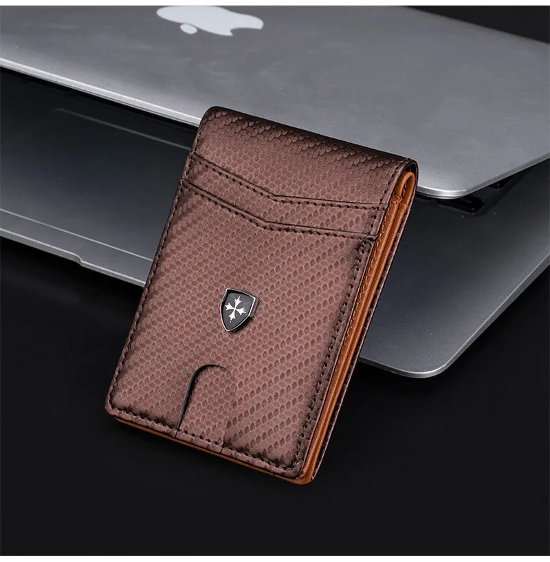A brown leather wallet with a money clip and a silver emblem is placed on a silver laptop.