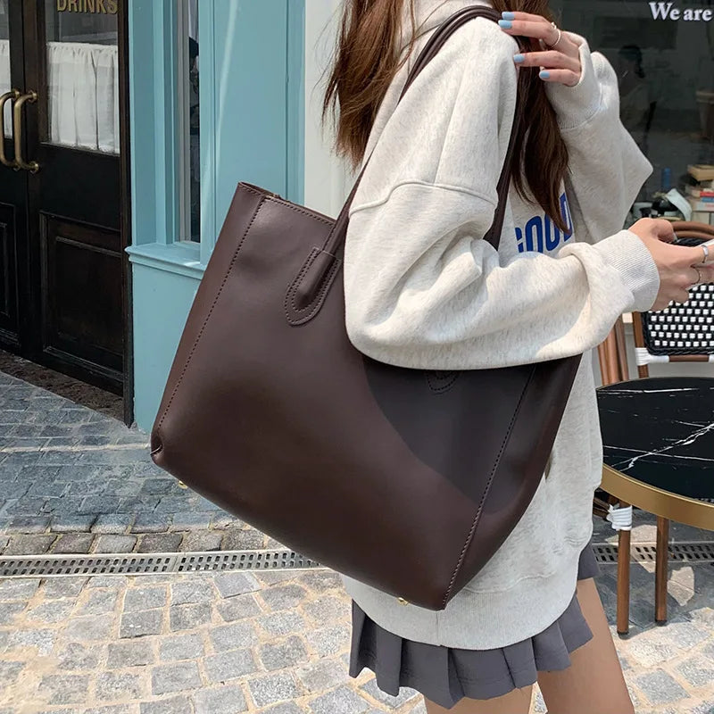 A woman wearing a light beige sweatshirt and a dark brown vintage large-capacity tote bag standing outside a storefront.