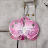 A realistic pink orchid flower keychain with purple veins and silver accents attached to a gray leather bag.