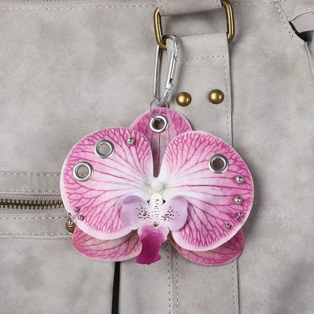 A realistic pink orchid flower keychain with purple veins and silver accents attached to a gray leather bag.
