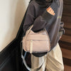 A person is holding a light pink multi-pocket nylon crossbody bag with a top handle against a dark background.