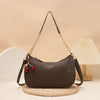 A dark brown leather shoulder bag with a gold chain and cherry pendant resting on a woven mat.