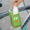 A hand is placing a white bottle into a green silicone cup holder attached to a bicycle frame.