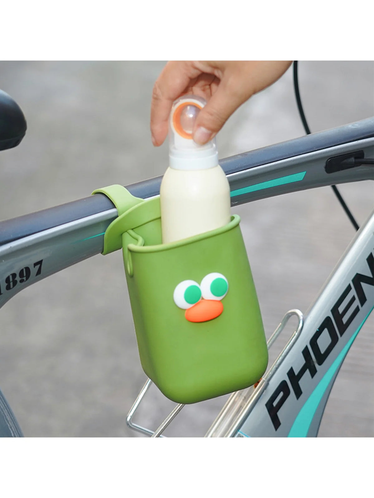 A hand is placing a white bottle into a green silicone cup holder attached to a bicycle frame.