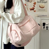 A pink canvas crossbody travel tote bag is shown being held by a person in a bright indoor setting.