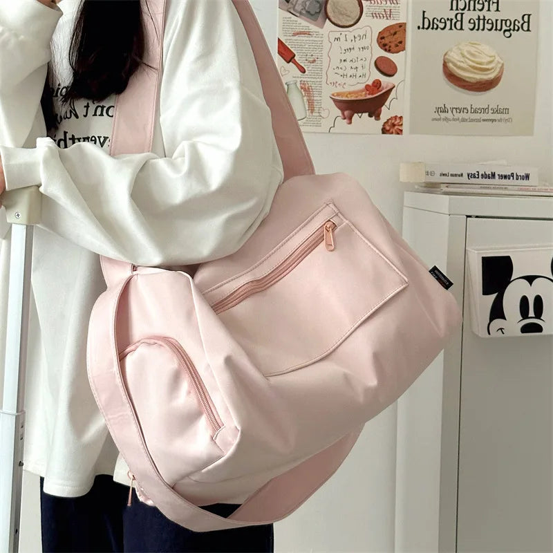 A pink canvas crossbody travel tote bag is shown being held by a person in a bright indoor setting.