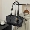 A black PU leather tote bag with gold hardware is hanging on a metal rack.