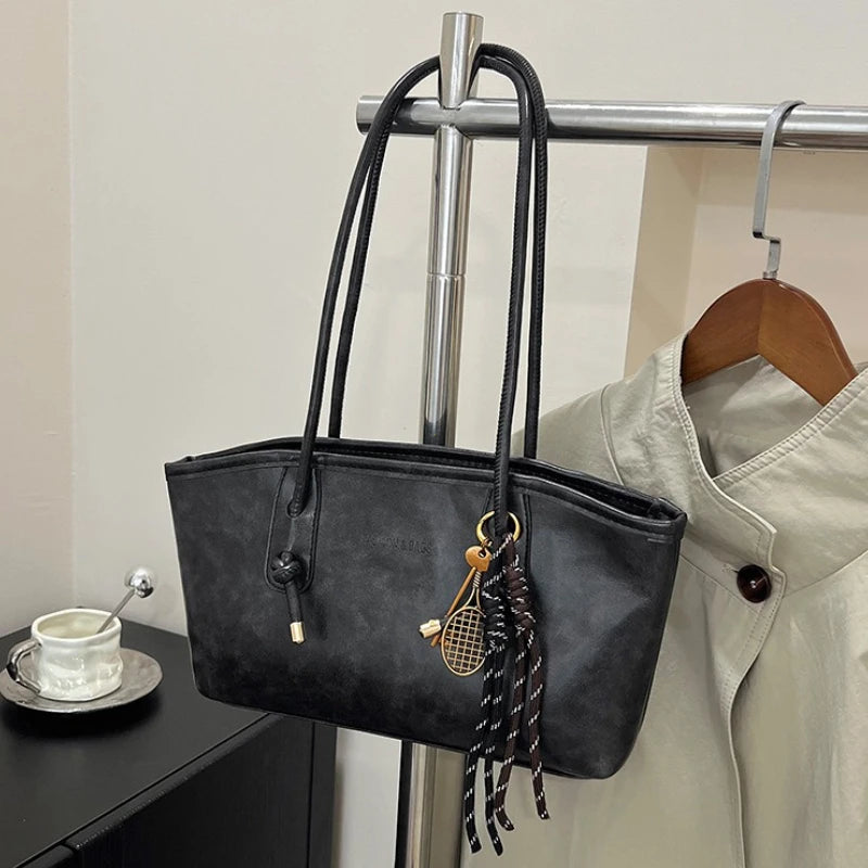 A black PU leather tote bag with gold hardware is hanging on a metal rack.
