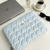 Light blue quilted laptop sleeve with a zipper and small silver perfume bottle on a white table.