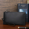 A black textured clutch bag is displayed next to a dark book and a pen on a wooden surface.