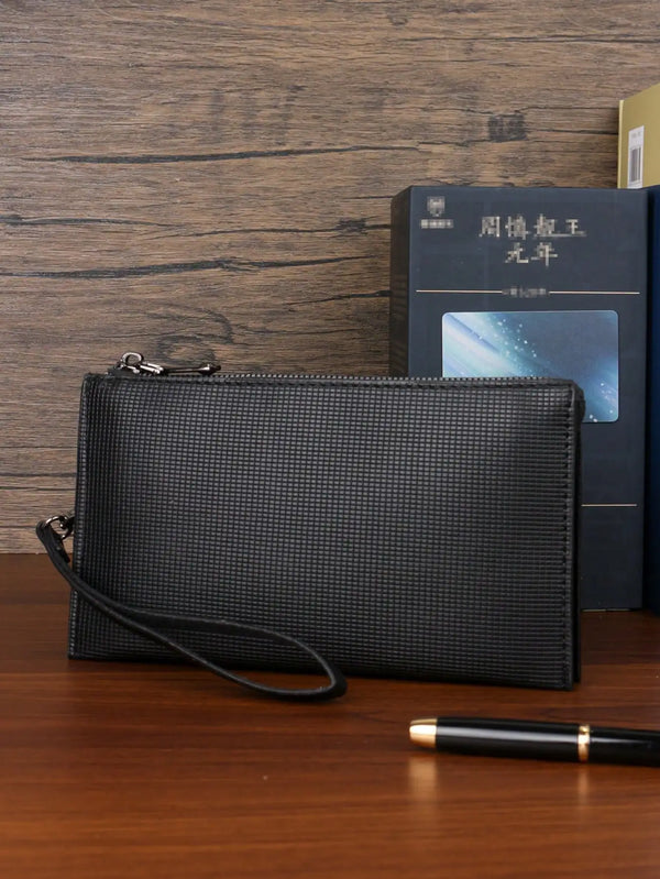 A black textured clutch bag is displayed next to a dark book and a pen on a wooden surface.
