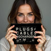 A woman holds a black zippered pouch labeled PLUGS CABLES & CHARGERS with various electronic accessories.