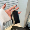 A hand holds a black nylon mini keychain tote bag with a gold clasp against a light background.
