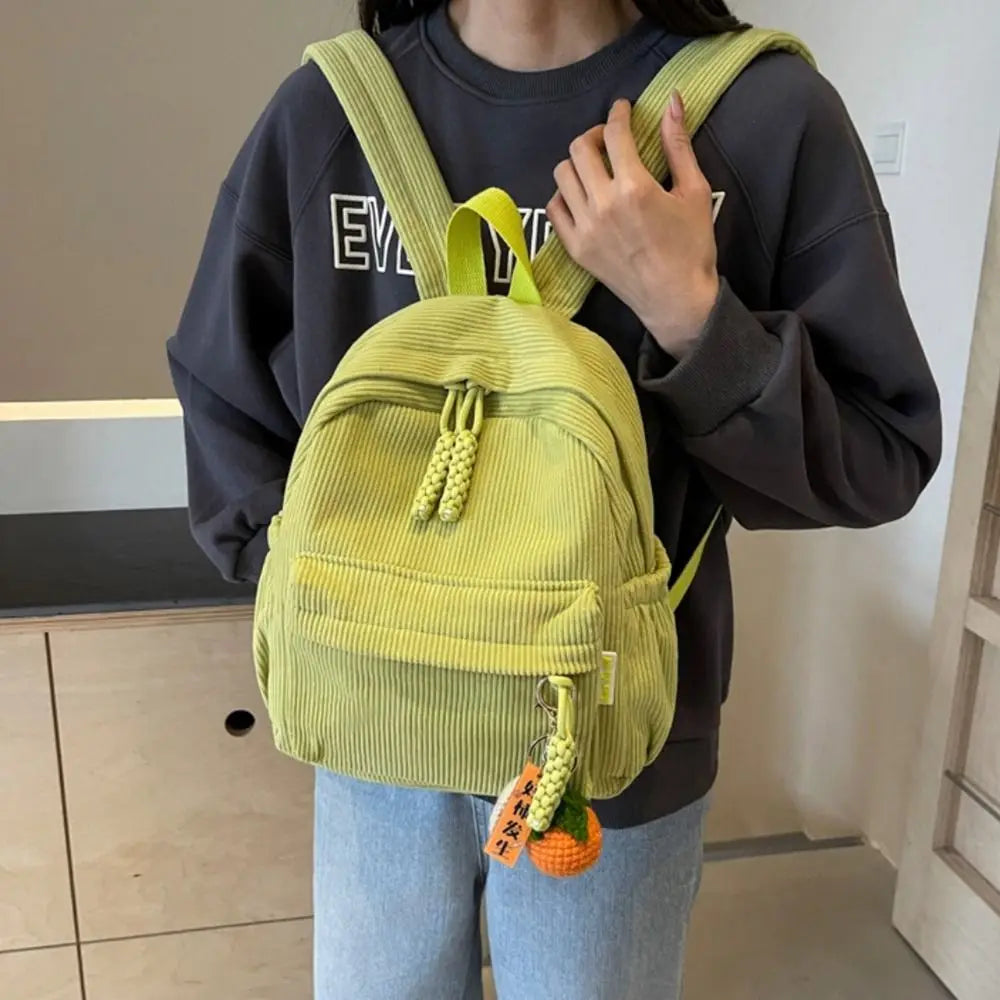 A person is holding a lime green corduroy daily backpack against a dark gray sweatshirt.