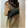 Una mujer modela un abrigo beige de gabardina y un bolso cruz de cuero negro.