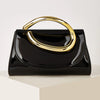A black leather clutch purse with a gold-toned handle is displayed on a light surface.