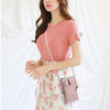 A woman wearing a pink t-shirt and floral dress carrying a mauve PU leather crossbody bag.