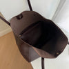 A dark brown vintage large-capacity tote bag hanging on a hook against a white wall.