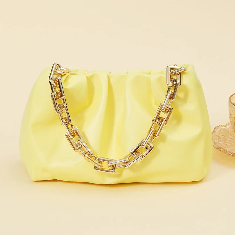 Cartera de acrílico amarillo pálido con correa de cadena dorada sobre un fondo claro.