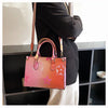 A pink and orange patterned ladies' shoulder tote bag carried by a person in a black blazer.