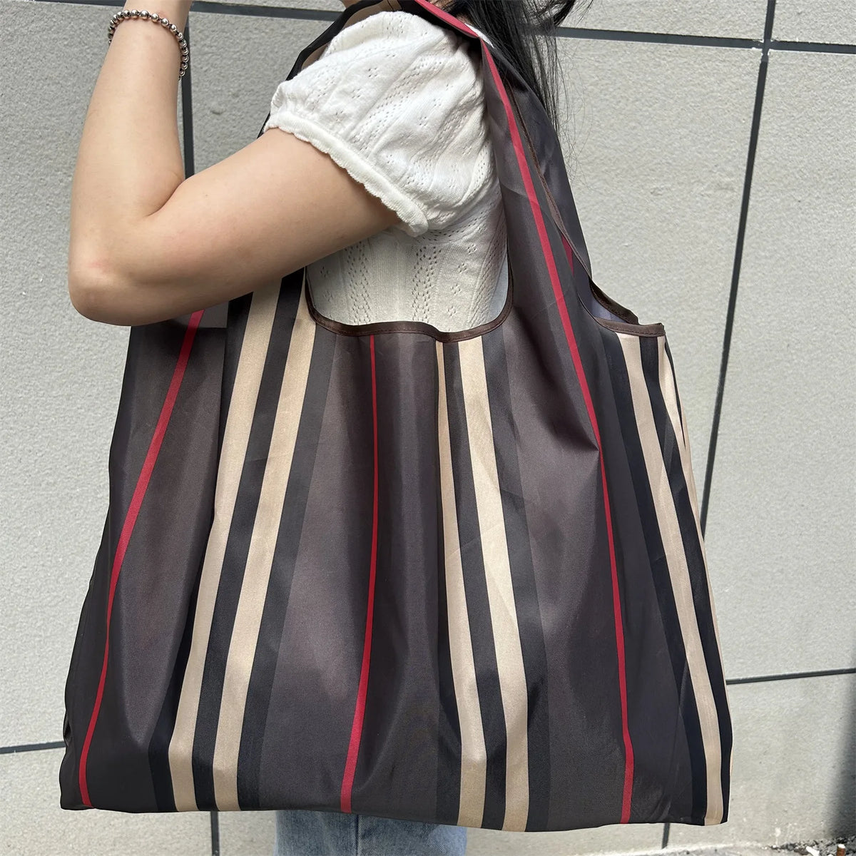 A person carrying a brown and beige striped foldable oxford grocery tote bag.