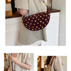 A woman wears a dark burgundy faux suede hobo crossbody bag with gold rivet accents over a beige shirt.
