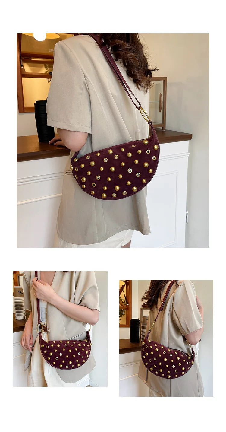 A woman wears a dark burgundy faux suede hobo crossbody bag with gold rivet accents over a beige shirt.