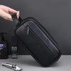 A black leather travel cosmetic bag is being held by a hand, next to a bottle and a metal tool.