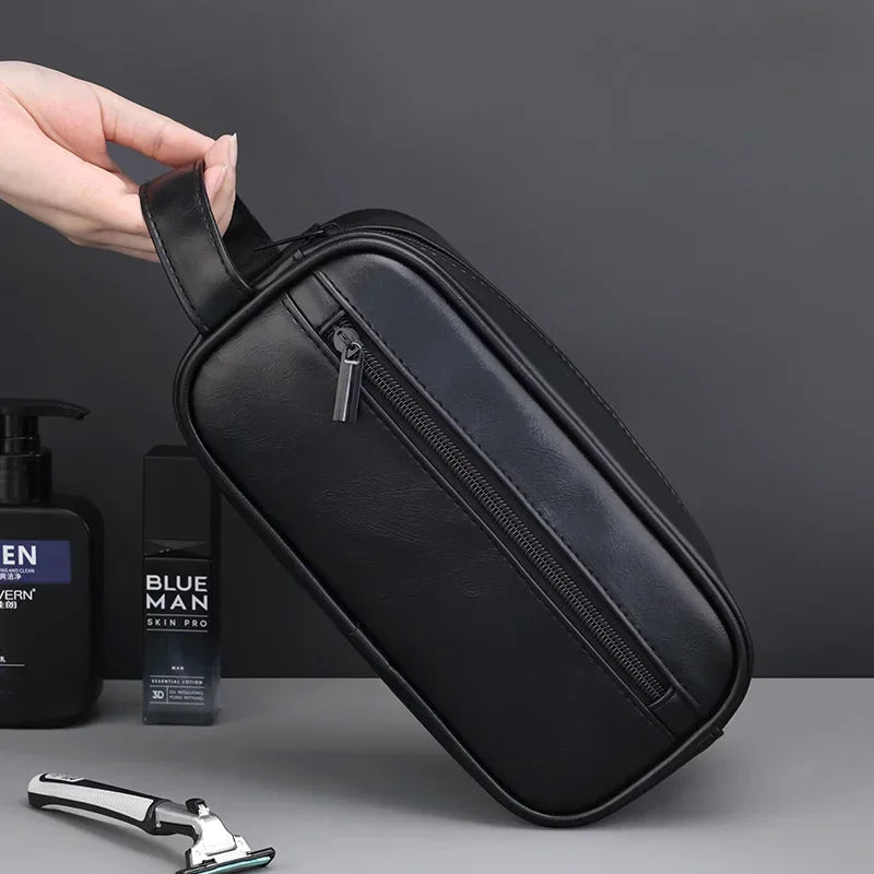 A black leather travel cosmetic bag is being held by a hand, next to a bottle and a metal tool.