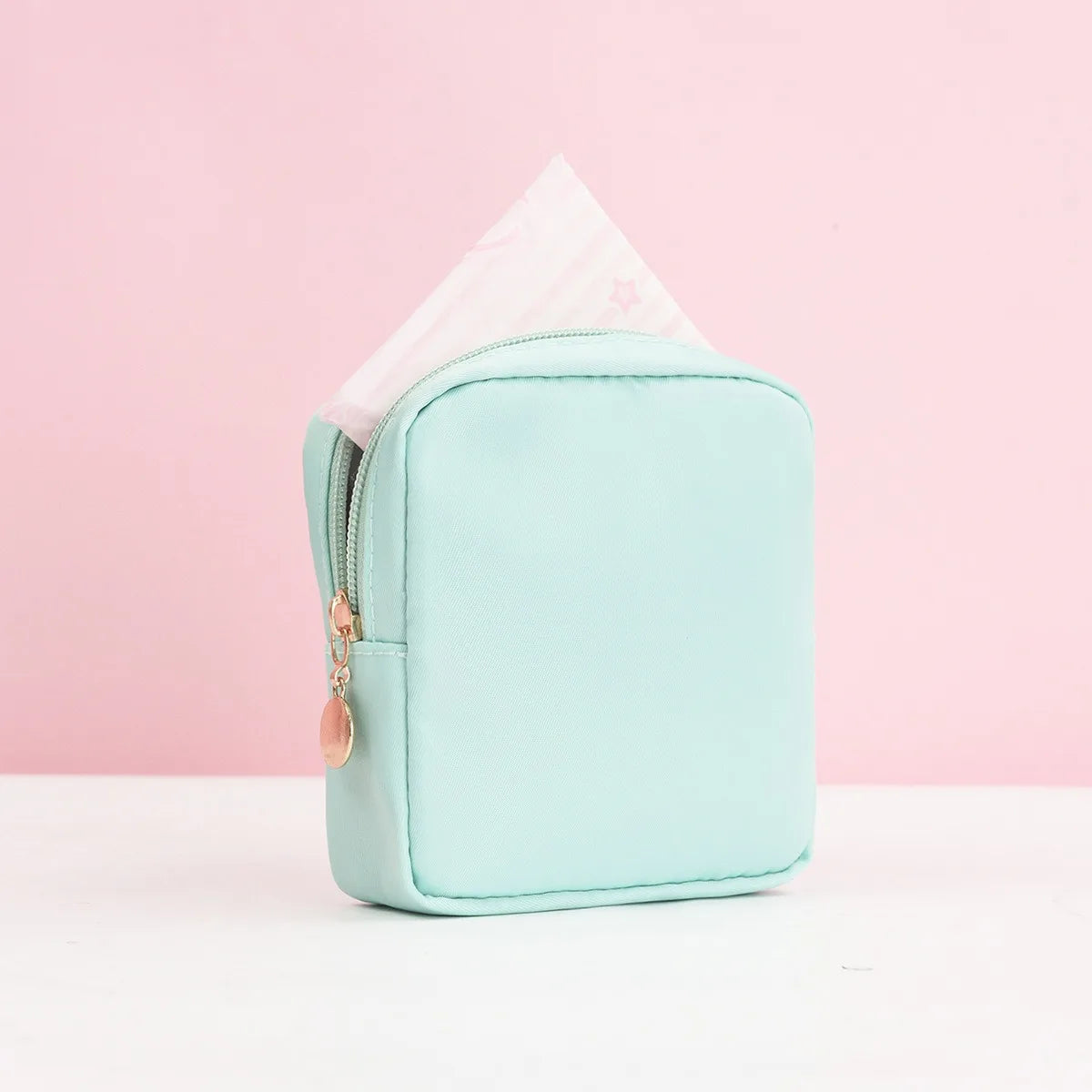 Eine mintgrüne tragbare Unterwegtasche mit rosa Dreieck-Abdeckung wird auf einer weißen Oberfläche präsentiert.