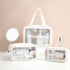 A clear waterproof travel toiletry bag with a white strap and multiple compartments is displayed on a white surface.
