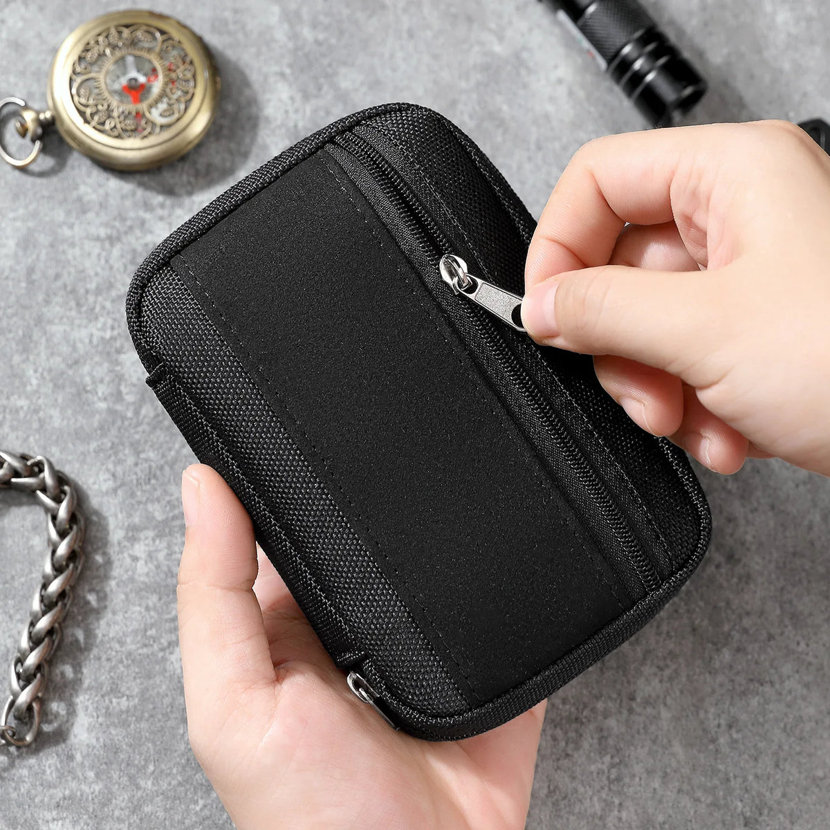 A hand holds a black portable multi-tool organizer pouch, showing the zippered compartment.