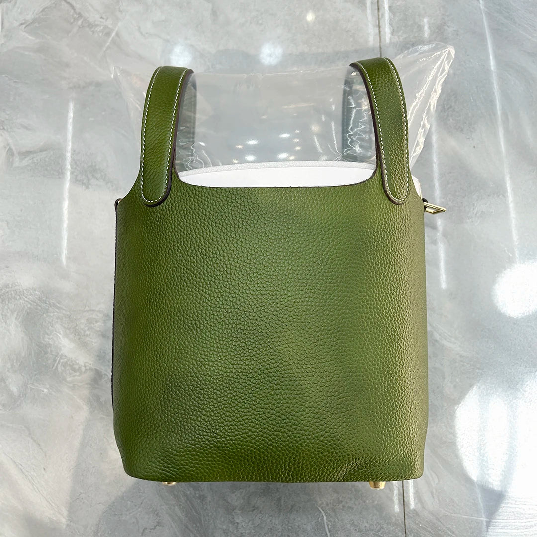 A olive green genuine leather bucket bag with a clear plastic cover is displayed on a reflective surface.