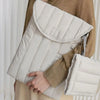 A beige knitted sweater is holding a light cream quilted laptop sleeve.
