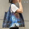 A woman holds a large, dark blue and black abstract painting shopping tote with a shoulder strap.