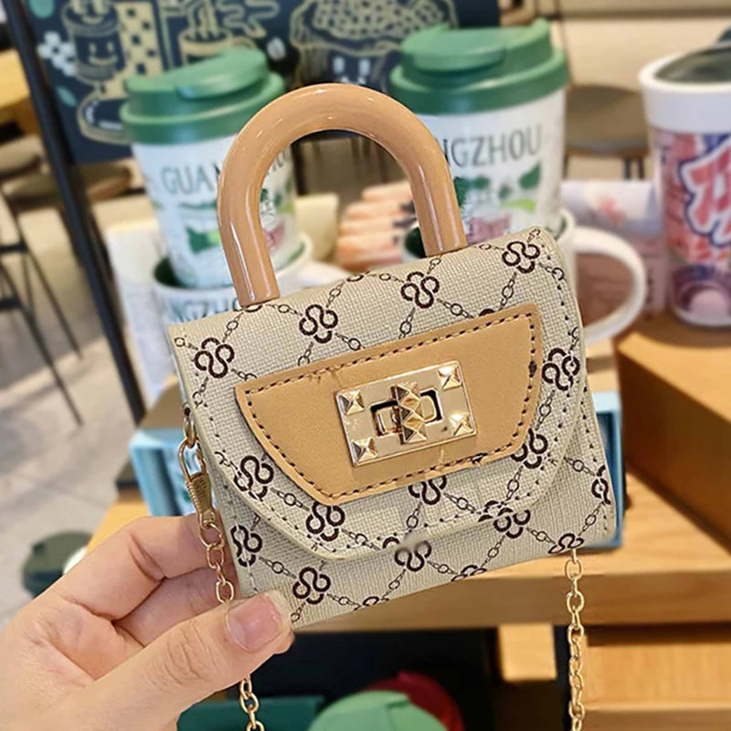 Bolso cruz de textura floral beige con solapa de cuero marrón claro y correa de cadena dorada, sostenido en la mano.