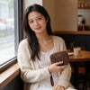 A woman wearing a cream cardigan holds a brown leather mini coin purse and card holder wallet.