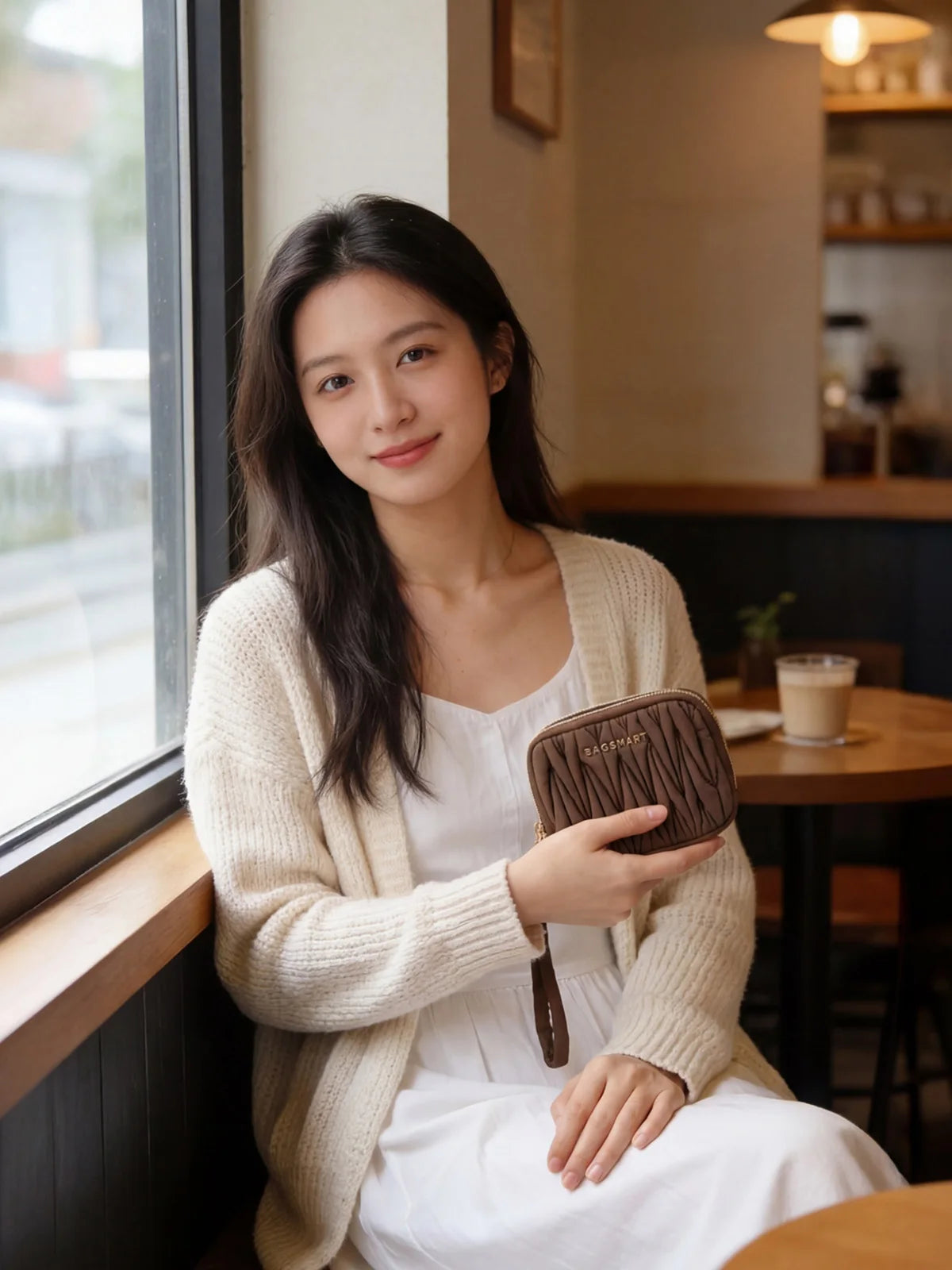 A woman wearing a cream cardigan holds a brown leather mini coin purse and card holder wallet.