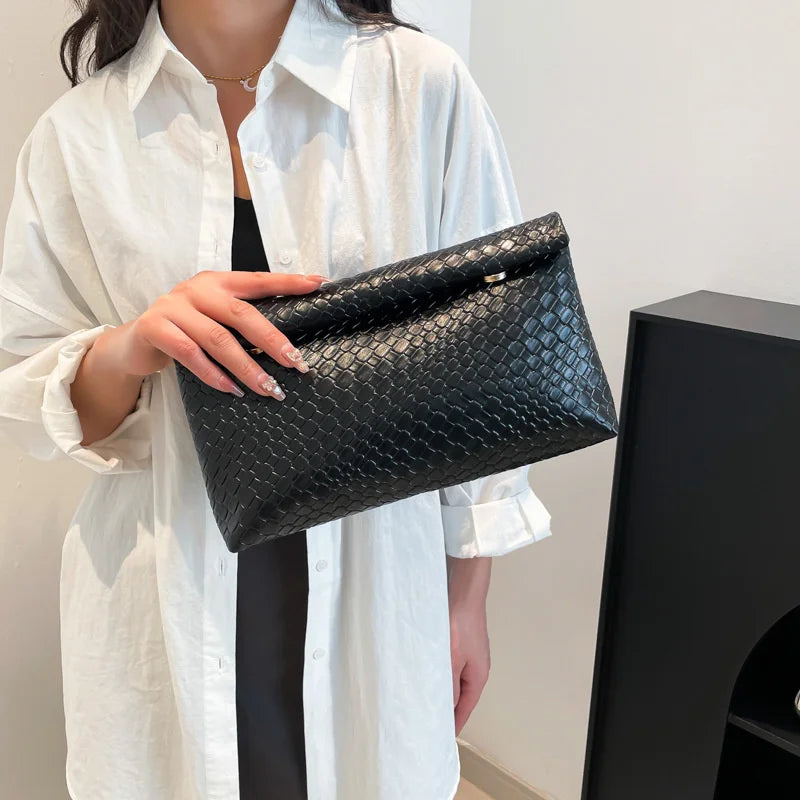 Una mujer sostiene un elegante bolso de mano tejido negro bajo una camisa blanca.