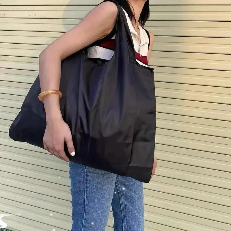 شخص يحمل حقيبة تسوق كبيرة سوداء قابلة للطي مع لمسات بيضاء وحمراء على الحزام.