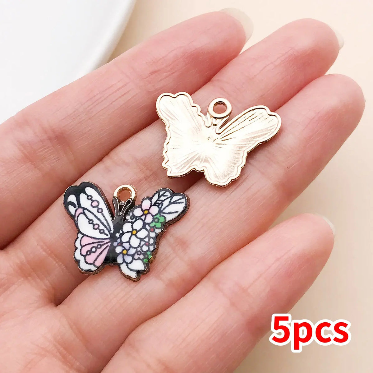 A set of five colorful butterfly enamel charms displayed on a person's hand.