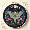 A circular embroidery hoop featuring a detailed floral and butterfly design in shades of green, pink, and dark blue thread.