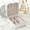 A white compact leather jewelry travel box with an open lid displaying multiple compartments.