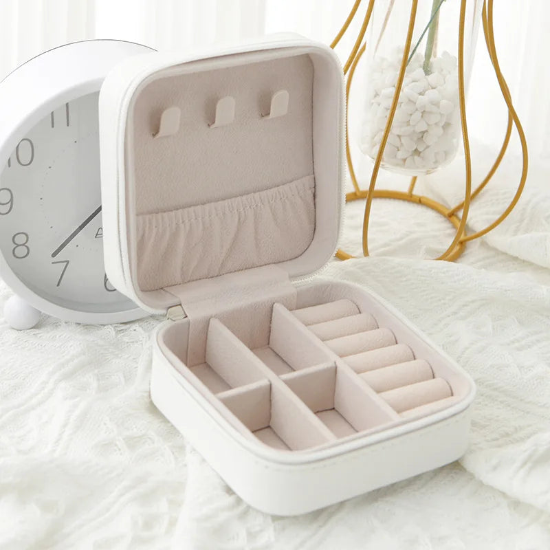 A white compact leather jewelry travel box with an open lid displaying multiple compartments.