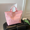 A pink and white striped waterproof PVC shoulder tote bag resting on a black leather surface.